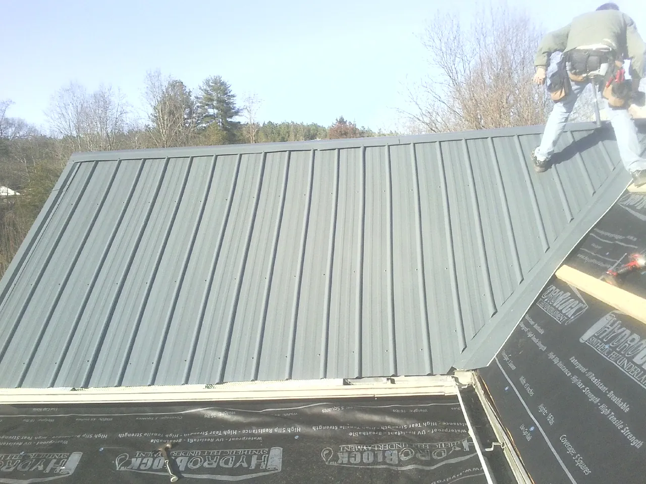 Crew installing dark green standing seam panels over synthetic underlayment in Hazel Crest